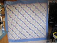 Front full view of the quilt hanging showing entire patchwork pattern and solid blue border.