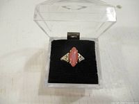 Clear top view of silver ring with pink stone in a plastic display box on a black cushion.
