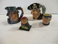 Four Royal Doulton character mugs and one figurine arranged on a white surface showing front views