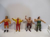 Photo showing three rubber wrestling figures standing side by side. Figures range in height from 7 to 8 inches, depicting muscular wrestlers in various wrestling outfits and colors.