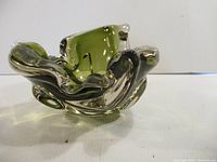 Side view of signed art glass with clear and olive green colors, with rounded, flowing shape.