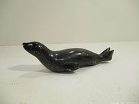 Side view of black soapstone seal sculpture showing polished surface and shape.