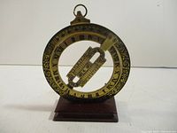Front view of the brass Universal Equinoctial Ring Dial showing detailed Roman numeral markings and ornate floral design on the ring, mounted on wooden base