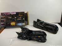 Front and side view of the 1989 Batman Batmobile toy car with matching cocoon cover and original box in background.