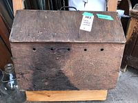 Side view showing wooden construction, ventilation holes near roof, handle on top, and overall shape of the carrier.