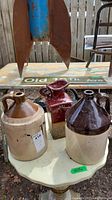 Three antique glazed pottery items on a small table outdoors, two crocks and one pitcher.