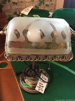 Front view of metal bankers lamp showing frosted glass shade with stamped decorative design and metal base with ornate detailing.