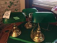 Three bankers lamps shown together on a table with visible brass bases and green shades.