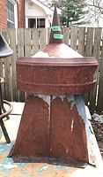 Front view of rustic metal barn roof vent showing rusted conical tip and base with peeling paint.