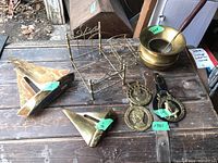 Overview showing 9 brass items including two sailboats, miniature bed frames, brass pot, and horse brasses on a rustic wood table.