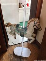 Side view of fibreglass carousel horse mounted on a white oval wood base with a vertical pole support.