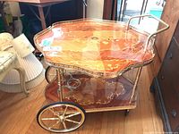 Three-quarter right side view showing octagonal shelves, drop leaf folded down, brass handle and large spoked wheel