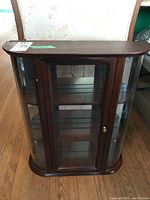 Front view of the wood veneer and glass display cabinet showing curved glass sides and door with brass knob.