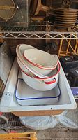 Three nested enamel roasting pans and bowls stacked inside a vintage rectangular enamel kitchen sink with blue rim.