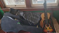 Photo showing two vintage acoustic guitars partially inside two hard black cases and one vinyl guitar case resting on a bench near a window.