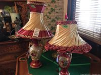 Pair of vintage Italian china lamps with original pleated cream and burgundy fabric shades on a wooden table near a window.