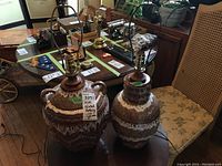 Pair of two glazed pottery lamps, brown and white speckled glaze with wooden necks, sitting on wooden surface without lamp shades.