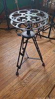 Overall view of black metal decorative occasional table with circular cutout pattern top and tripod legs on wood floor.