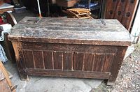 Front view of closed wooden trunk showing weathered dark wood with vertical panel detailing and block feet.