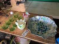 Overview of lot showing signed Vaseline glass bowl, two art glass vases, and eight green glass cups on a table.