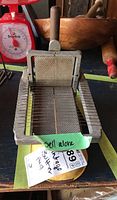 Top-down photo of the vintage butter pad slicer, showing the metal grid and wooden handle on cast metal base with minor rust spots.