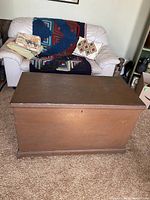 Closed view of antique solid wood blanket box with lift top lid in front of couch.
