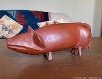 Front-left angled view of the carved red wood pig, showing the stylized carved eyes, ears, and overall smooth rounded body shape.