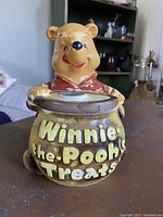 Front view of the ceramic cookie jar showing Winnie the Pooh head lid and the pot with raised text.