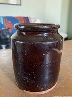 Front view of antique Albany slip glaze crock showing the dark brown glossy finish and cylindrical body.