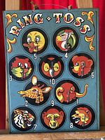 Front view of colourful antique ring toss game board showing painted animal faces and metal pegs.