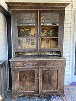 Front view of two-piece wooden cupboard on porch, showing upper glass doors and lower paneled doors