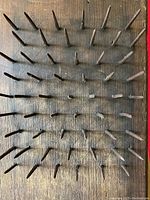 Close-up photo showing square nails mounted on wooden hetchel board surface.