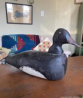 Side view of large, black wooden goose decoy showing texture and paint condition.