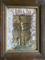 Front view of antique shadow box featuring crucifixion scene inside wooden frame with pink satin lining and white flowers.