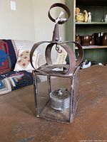 Antique oil lamp with metal crown-like frame, loop handle, and glass panels showing patina and wear