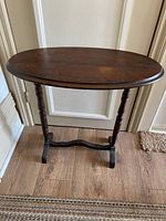 Full view of antique walnut oval accent table with spindle legs and stretcher base on wood floor near white wall and door.
