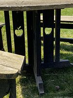 Photo showing black wooden table legs with apple-shaped cut-outs and part of bench leg also showing apple cut-out.