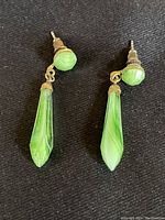 Front view of the jade earrings laid flat on black fabric, showing the round stud and long teardrop dangle.