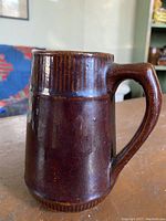 Front and side view of dark brown glazed pottery pitcher with ribbed textured bands near top and bottom, and handle