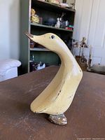 Front angled view of the hand carved wooden duck showing yellow paint with some wear, black eyes, and brown detailing on beak and base.