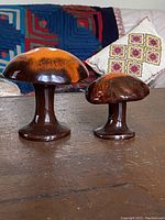 Two ceramic orange brown pottery mushrooms placed on a wooden surface, showing overall appearance and color.
