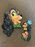 Front view of three chalkware Cocker Spaniel dog head wall hangings in cartoon style, featuring large colorful eyes, bow ties, and a flower.
