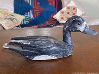 Side angled view of the carved wooden duck decoy showing black and white paint with realistic glass eye.
