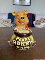 Front view of the ceramic Winnie The Pooh honey bank showing Pooh holding honey pot with embossed text.