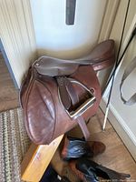 Photo of vintage Harmony brown leather horse saddle positioned over a wooden stand with stirrups and brown leather riding boots beneath.
