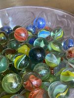 Close-up photo of a collection of round glass marbles with colorful swirls inside in a decorative dish.