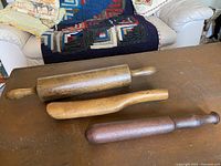 Three wooden kitchen tools on a table including two rolling pins and one dark wooden mallet.