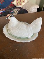 View of the milk glass hen on nest covered dish from the right front angle showing textured body and painted comb and eyes.
