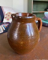 Front and side view of brown glazed redware jug with handle and small spout, showing glossy surface and shape.