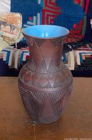 Front view of the pottery vase showing intricate carved geometric patterns and blue glazed interior.